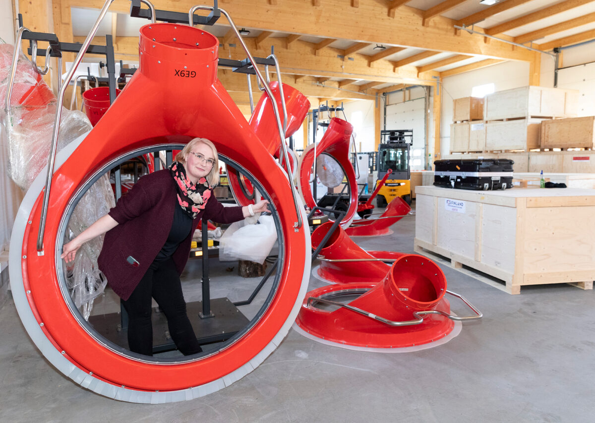 Nina Koskinen antaa mittakaavaa sille, kuinka suuria suihkumoottorit ovat. Renkaan muotoinen adapteri kiinnittyy moottorin pakoputkeen.